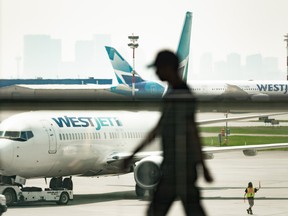 A person walks by as a WestJet Airlines Ltd. plane gets ready for take-off at Calgary International Airport.
