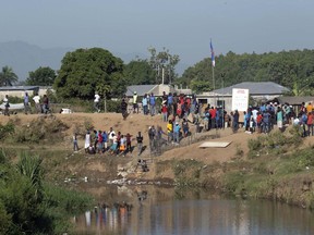 People watch from the bank of the Massacre River as workers build a canal that reaches the river, the natural border between Haiti and the Dominican Republic, photographed from Dajabon, Dominican Republic, Friday, Sept. 15, 2023. The Dominican Republic shut all land, air and sea borders with Haiti on Friday in a dispute about construction of a canal on Haitian soil that taps into the shared river.