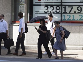FILE - People walk in front of an electronic stock board showing Japan's Nikkei 225 index at a securities firm on Sept. 5, 2023, in Tokyo. Shares fell Friday, Sept. 8 in Asia after Japan reported its economy grew less than earlier estimated in the last quarter.