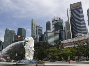 FILE - People are dwarfed against the financial skyline as they take photos of the Merlion statue along the Marina Bay area in Singapore, on June 30, 2020. Singapore police uncovered more luxury watches, gold bars and other assets from a massive money laundering scheme that was busted August 2023, they said, bringing the total amount of assets seized or frozen to 2.4 billion Singapore dollars ($1.75 billion).