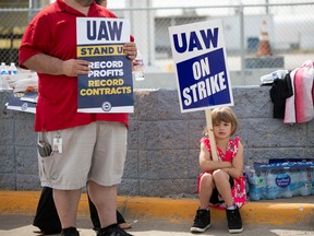 A young supporter holds a sign as United Auto Workers members strike at a Ford assembly plant in Wayne, Mich.