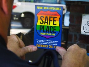 FILE - In this June 24, 2015 photo, Officer Jim Ritter places a "Safe Place" sticker on the window of a business in Seattle's Capitol Hill neighborhood. Some central Florida lawmakers said they are considering "all legislative, legal and executive options available" to stop business owners in a small town from voluntarily displaying rainbow decals in their windows indicating that they are "safe places" for LGBTQ people who feel threatened.