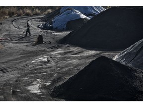 A man walks past piles of coal at the Qinhuangdao Port in Qinhuangdao, China, on Friday, Oct. 28, 2016. China's efforts to quell surging coal prices showed signs they're working, with benchmark prices dropping for the first time in a year as the country's production rose to the highest in seven months. Photographer: Qilai Shen/Bloomberg