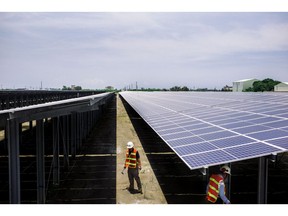 Workers stand next to solar panels at a Vena Energy solar-power installation in Yunlin County, Taiwan.