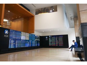 A man looks at his phone as an electronic board displays stock information at the Australian Securities Exchange, operated by ASX Ltd., in Sydney, Australia, on Monday, May 20, 2019. Prime Minister Scott Morrison's center-right government will command a parliamentary majority, the Australian Broadcasting Corp. projected Monday, fueling a stock market rally as investors welcomed his surprise victory in the weekend election.