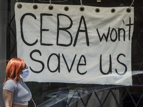 A pedestrian walks past a store on Toronto's Dundas Street West stating 'CEBA Won't Help Us' during the COVID-19 pandemic, 2020.