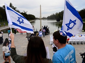 People wave flags of Israel as a "Shabbat Dinner" table is prepared with 200 empty seats representing the Israeli hostages and missing people at the Lincoln Memorial in Washington, DC.