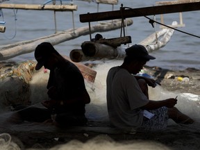 FILE - Fishermen work on nets as they spend time on the shores of their coastal village in Cavite province, south of Manila, Philippines, on May 7, 2020. Canada will help the Philippines detect illegal fishing with its satellite surveillance system under a new agreement, Philippine officials said Monday, Oct. 16, 2023.