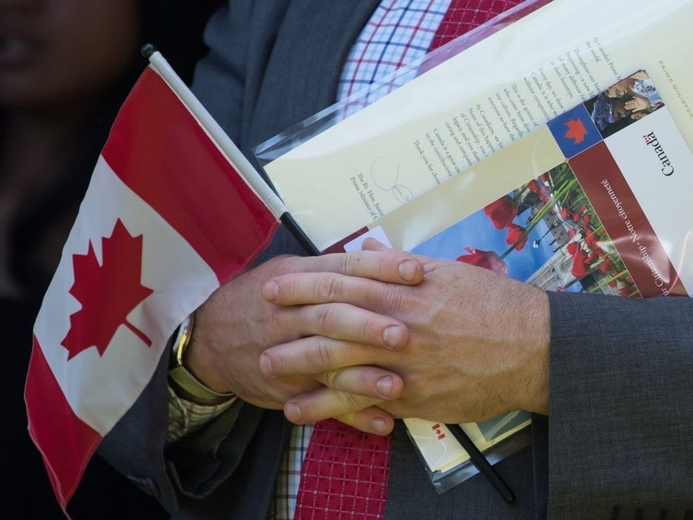 A new Canadian holds a Canadian flag, their citizenship certificate and a letter signed by Prime Minister Justin Trudeau as they sing O Canada after becoming a Canadian citizen, during a special Canada Day citizenship ceremony in West Vancouver on Monday, July 1, 2019. 