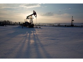 An oil pumping jack, also known as a 'nodding donkey,' operates in a snow covered oilfield near a derrick, right, during drilling operations in an oilfield operated by Bashneft PAO in the village of Otrada, 150kms from Ufa, Russia, on Saturday, March 5, 2016.  Photographer: Andrey Rudakov/Bloomberg