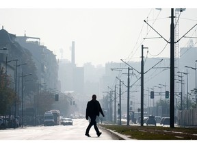 A pedestrian crosses a street in heavy smog in Belgrade, Serbia, on Tuesday, Nov. 1, 2022. Smog spewing from ancient coal-fired power plants, outdated automobiles and heating systems running on burning tires and wood is choking the Balkans both literally and economically.