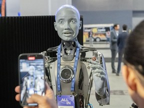 People take photos of an AI robot at the All In artificial intelligence conference, Wednesday, September 27, 2023 in Montreal. A company that specializes in protecting phone users from spam says it expects generative artificial intelligence to drastically change the way call recipients are targeted.
