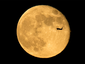 An airplne is silhouetted against the moon.