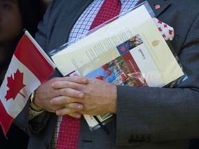 A new Canadian holds a Canadian flag, their citizenship certificate and a letter signed by Prime Minister Justin Trudeau during a Canada Day citizenship ceremony in West Vancouver.