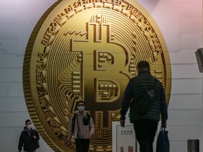 Pedestrians walk past an advertisement displaying a Bitcoin cryptocurrency token in Hong Kong, China.