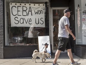 A pedestrian walking his dog walks past a store on Toronto’s Dundas Street West stating 'CEBA Won’t Help Us' in 2020.