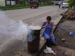 A Sri Lankan woman blows air to fire a hearth to boil sweet corn before selling them by a roadside in Colombo, Sri Lanka, Wednesday, Dec. 6, 2023. The woman has resorted to the roadside trading after her husband lost his job in the economic crisis.