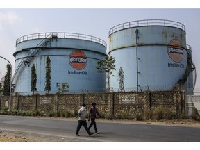 Pedestrians walk along a road past storage tanks in a Indian Oil Corp. facility near Jawaharlal Nehru Port, operated by Jawaharlal Nehru Port Trust (JNPT), in Navi Mumbai, Maharashtra, India, on Monday, March 30, 2020. As billions of people stay home in the the world's major economic centers, consumption of everything from transport fuel to petrochemical feedstocks is in freefall. Refiners that have already been filling up their storage tanks with unsold products now have little choice but to partially shut down their plants.