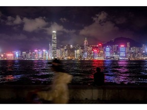 A pedestrian walks along a promenade in front of the city's skyline in Hong Kong, China, on Tuesday, Dec. 7, 2021. Hong Kong will prioritize quarantine-free travel for business people when its China border reopens, Chief Executive Carrie Lam said, warning that the city's vaccination rate could curb a broader roll-out. Photographer: Paul Yeung/Bloomberg