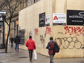 Shoppers walk past a boarded up storefront on Saint-Catherine Street in downtown Montreal.