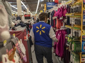 An employee walks through clothes displayed for sale at a Walmart. The retailer is increasing pay and incentives for store managers.