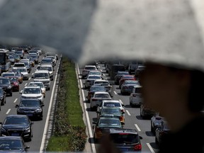 FILE - A woman walks past vehicles on a city ring-road clogged with heavy traffic in Beijing on Aug. 13, 2019. China's auto exports surged 63.7% in 2023 while sales at home, boosted by year-end incentives, rose 4.2%, an industry association said Thursday, Jan. 11.