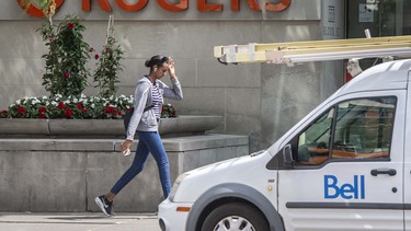 A pedestrian walks past the Rogers Communications Inc. moniker with a Bell truck in the foreground.