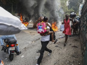 People walk past burning tires during a protest against Haitian Prime Minister Ariel Henry in Port-au-Prince, Haiti, Monday, Feb. 5, 2024. Banks, schools and government agencies closed in Haiti's northern and southern regions on Monday while protesters blocked main routes with blazing tires and paralyzed public transportation, according to local media reports.