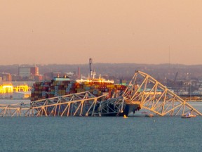 The steel frame of the Francis Scott Key Bridge sits on top of a container ship after it struck the bridge in Baltimore, Maryland, on March 26, 2024.