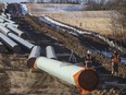 Workers survey around pipe to start construction for the Trans Mountain expansion project in Acheson, Alta.