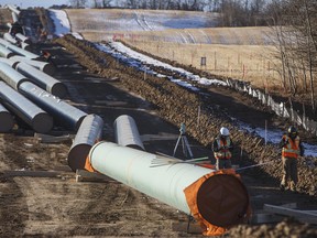 Workers survey around pipe to start construction for the Trans Mountain expansion project in Acheson, Alta.