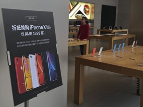 FILE - A trade-in for iPhone XR promotion board is displayed as an Apple employee waits for customers at its retail store in Beijing, Thursday, Jan. 3, 2019. Apple has agreed to pay $490 million to settle a class-action lawsuit alleging CEO Tim Cook misled investors about a steep downturn in the iPhone's sales in China that culminated in a jarring revision to the company's revenue forecast. The preliminary settlement was filed Friday, March 15, 2024, in Oakland, Calif., federal court.