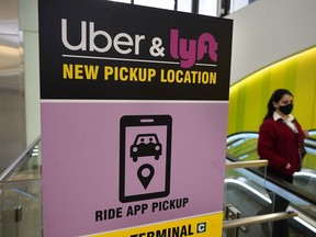 FILE - In this Feb. 9, 2021 file photo, a passer-by walks past a sign offering directions to an Uber and Lyft ride pickup location at Logan International Airport, in Boston. Lyft and Uber are threatening to halt operations in Minneapolis because of a city ordinance to increase wages for app-based drivers, the latest back-and-forth that underscores a longtime fight between gig economy workers and the tech giants.