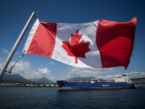 A Canadian flag flies from a Harbour Authority patrol boat as an oil tanker is guided by tugboats out of the Port of Vancouver.