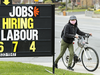A woman on a bicyle passes a hiring sign