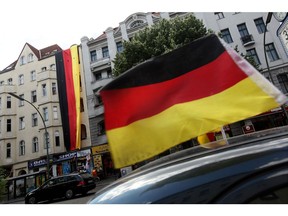 BERLIN - JUNE 29:  A car decorated with a German flag drives past a four-storey long German flag hanging over the electronics shop of local Muslim resident Youssef Bassal on June 29, 2010 in Berlin, Germany. Bassal, who's shop is in Sonnenallee street in a section of Kreuzberg distric heavily populated by Turks and Arabs, says he hung the flag to show his support for the German national soccer team in the FIFA 2010 World Cup, and he claims he has since received threats demanding he take the flag down and endured at least three instances of radical, left-wing Germans trying to burn or tear the flag down in the last week.