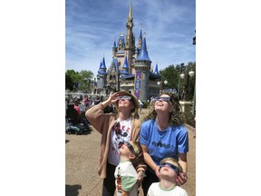 A family visiting from Sarasota watches the solar eclipse at the Magic Kingdom at Walt Disney World, in Lake Buena Vista, Fla., Monday, April 8, 2024.