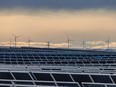 Solar panels at the Travers Solar Project with wind turbines behind them, west of Lomond, Alta.