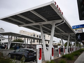 Tesla electric vehicles charge on EV charging stations beneath solar panels at a Tesla Supercharger location in Santa Monica, California.