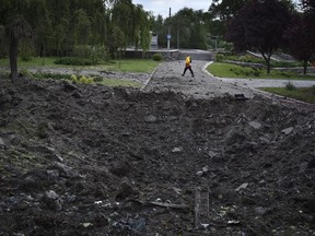 A woman walks in front of a crater caused by a Russian missile attack in Zaporizhzhia, Ukraine, Wednesday, May 8, 2024.