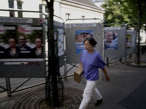A woman walks past a campaign site for the upcoming parliamentary elections in Paris, Thursday, June 27, 2024. Voters will choose members of parliament for the National Assembly in two rounds on June 30 and July 7.