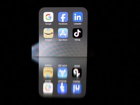 This photo taken on Feb. 12, 2023 in Brussels shows reflexions on a smartphone screen of logos of online platforms Google, Facebook, LinkedIn, Amazon, Apple store and Tiktok.