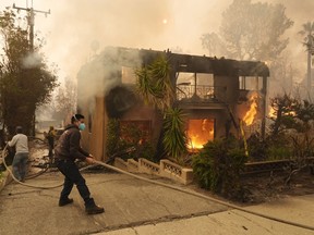 Pejalan kaki membantu petugas pemadam kebakaran meregangkan selang saat gedung apartemen terbakar, Rabu, 8 Januari 2025, di kawasan Altadena, Pasadena, California.