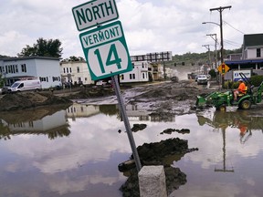 FILE - A small tractor clears water from a business as flood waters block a street, July 12, 2023, in Barre, Vt.