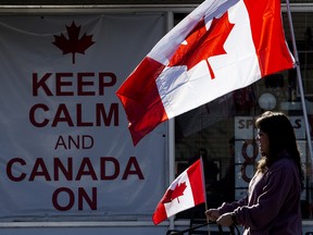 A pedestrian makes their way past flags and a 'keep calm and Canada on' sign outside O'Canada Gear in Edmonton, Alta.