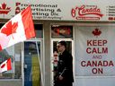 A pedestrian makes their way past flags and a 'keep calm and Canada on' sign outside O'Canada Gear in Edmonton, Alta.