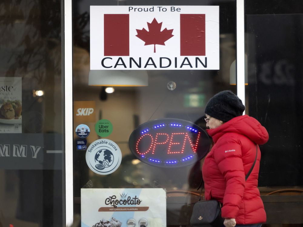 Seorang pembelanja berjalan melewati toko Oakville dengan papan nama yang menyatakan 'bangga menjadi Kanada' dengan bendera Kanada.