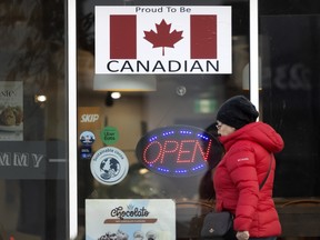 Seorang pembelanja berjalan melewati toko Oakville dengan papan nama yang menyatakan 'bangga menjadi Kanada' dengan bendera Kanada.