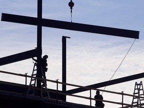 Workers position steel beams atop a building under construction along Dundas Street West in Belleville, Ont. March 9, 2021.