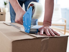 Close-up of young man while he is packing a cardboard box with scotch-tape and preparing to move house.